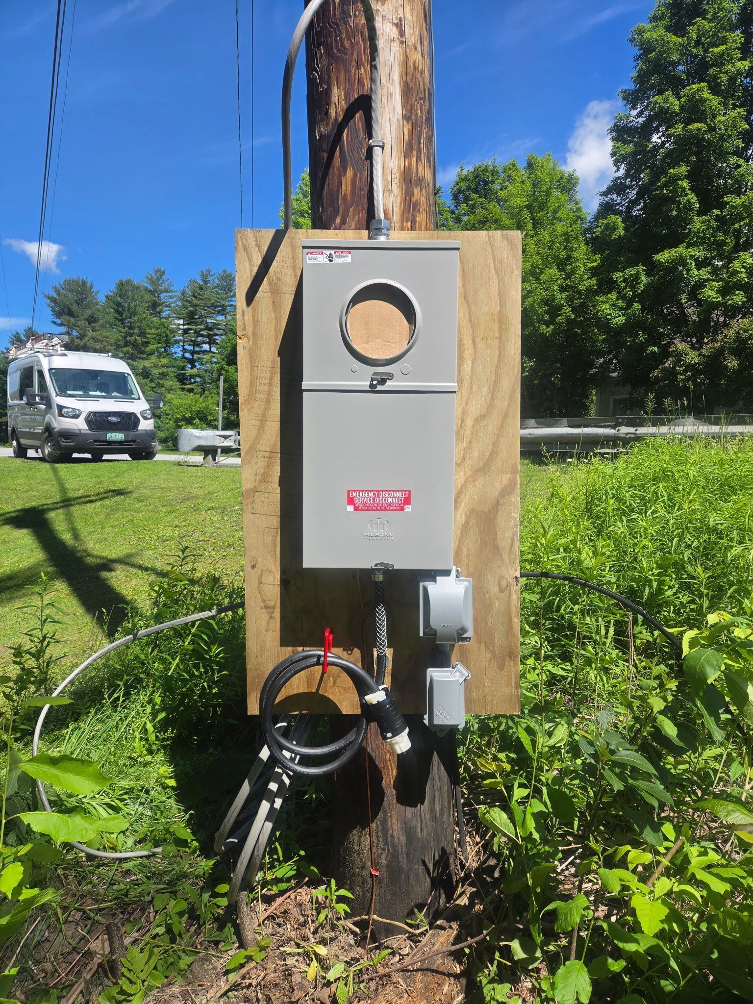Gray electrical box mounted on a tree in a grassy yard, with cables and equipment attached.