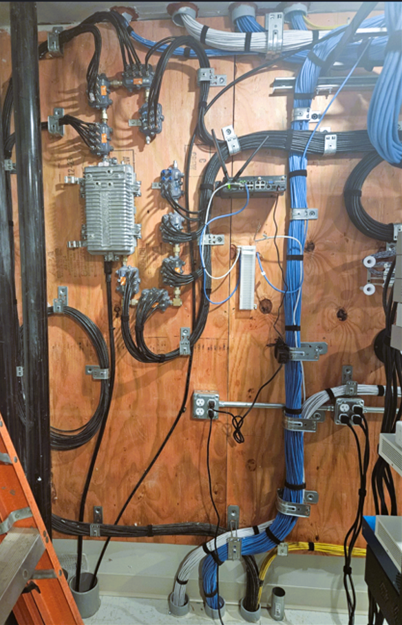 Wooden wall with tangled cables, pipes, and mounted electrical/mechanical components in a utility space.