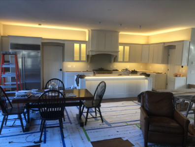 Modern white kitchen with island, dining table, and brown armchair in warm lighting