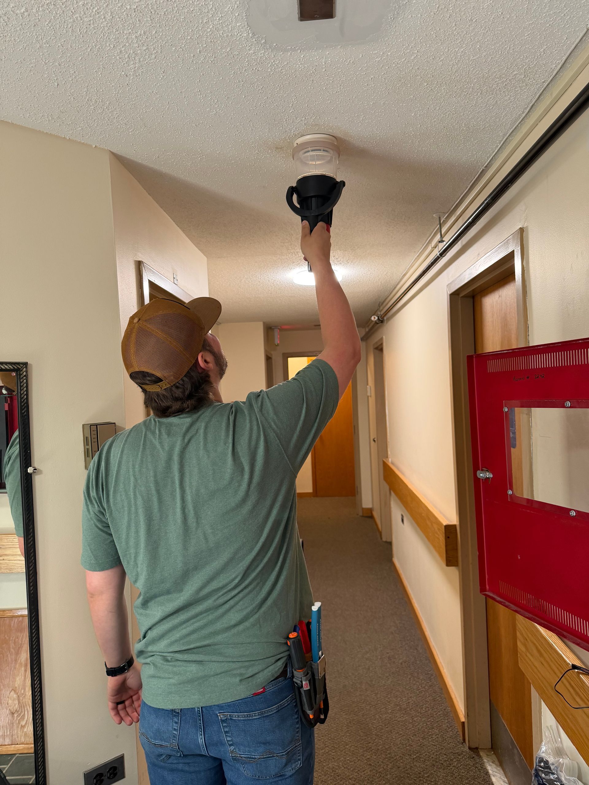 Technician installing a smoke detector in a residential hallway