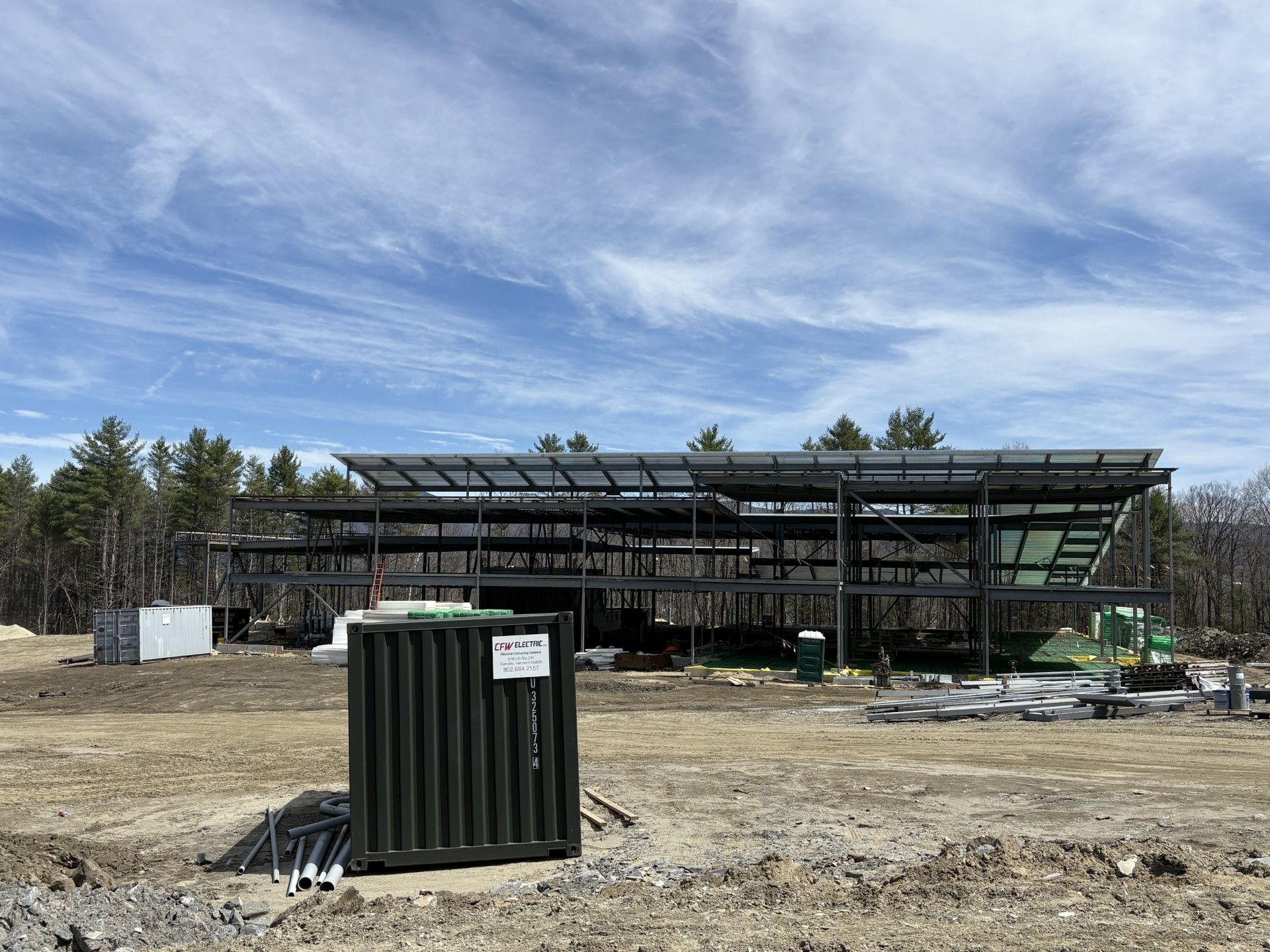 Construction site with steel frame building under construction and a green utility container in the foreground