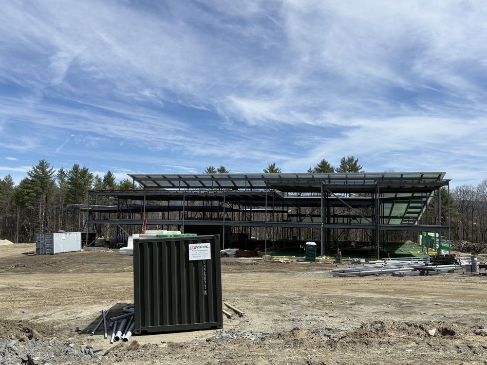 Construction site with steel frame building under construction and a green utility container in the foreground