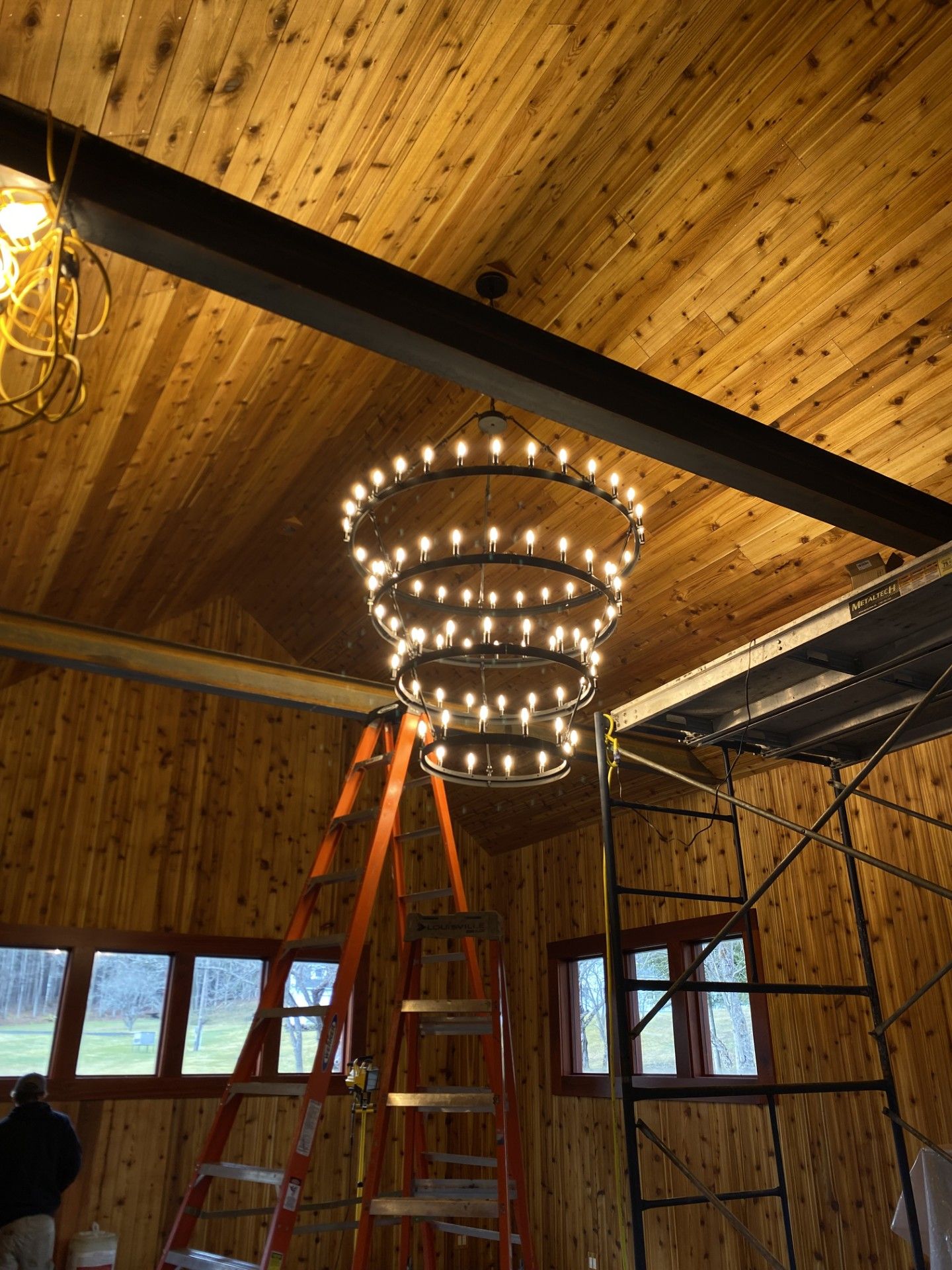 Ladder and chandelier under a wood-paneled ceiling in a barn-like room under construction