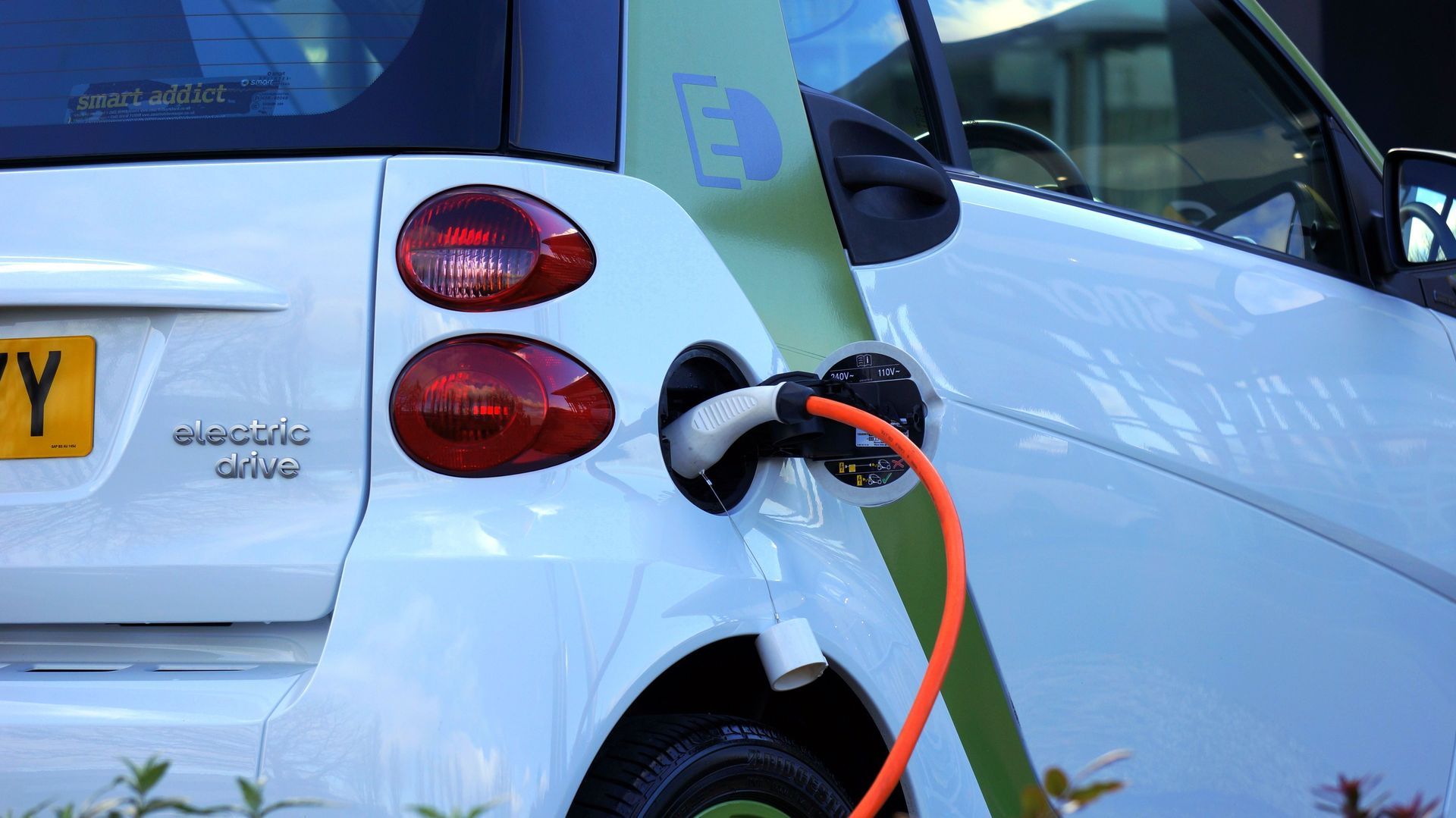 White electric car charging at a station with an orange cable plugged in.