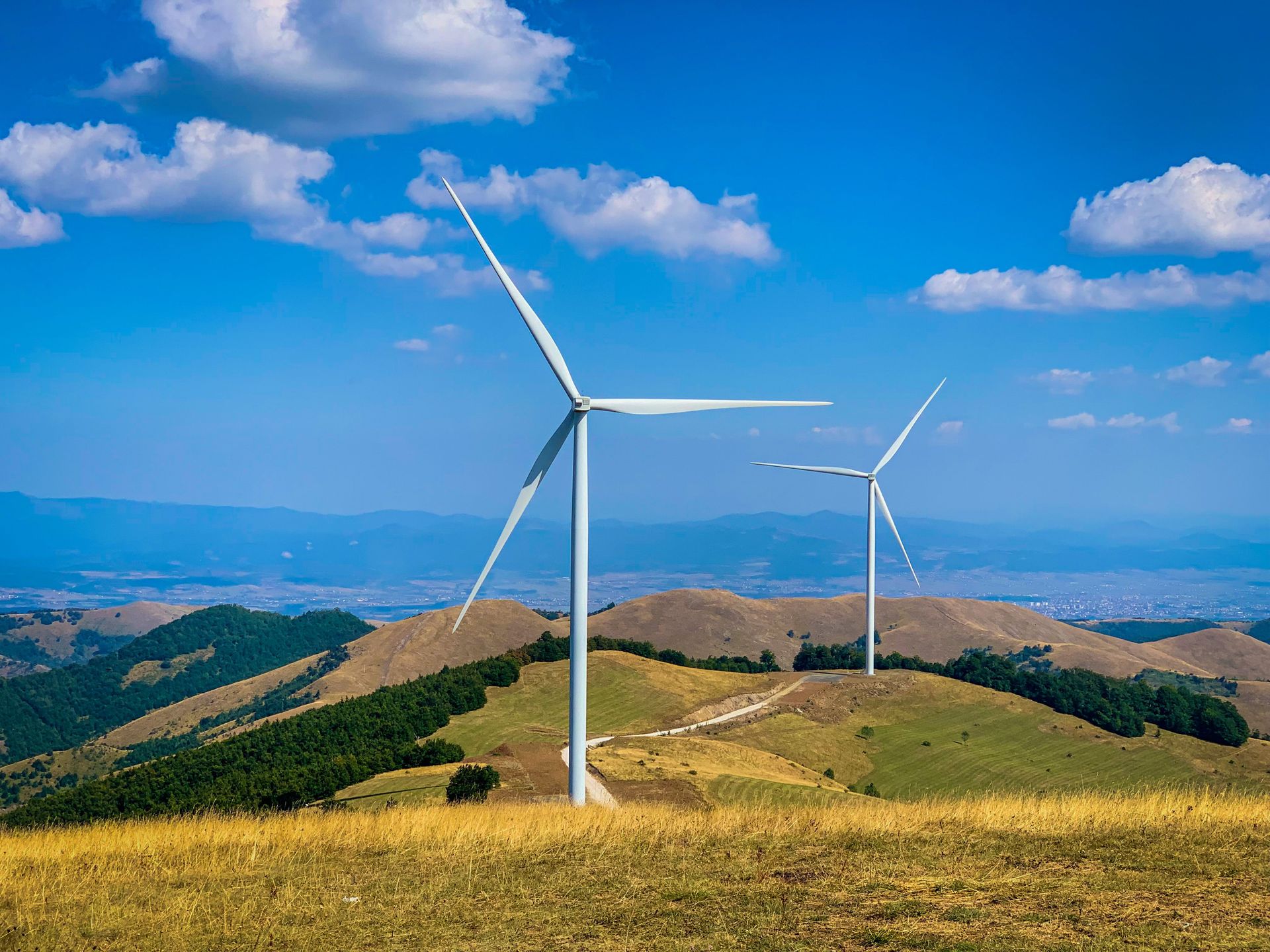 Wind turbines on grassy hills under a blue sky with clouds