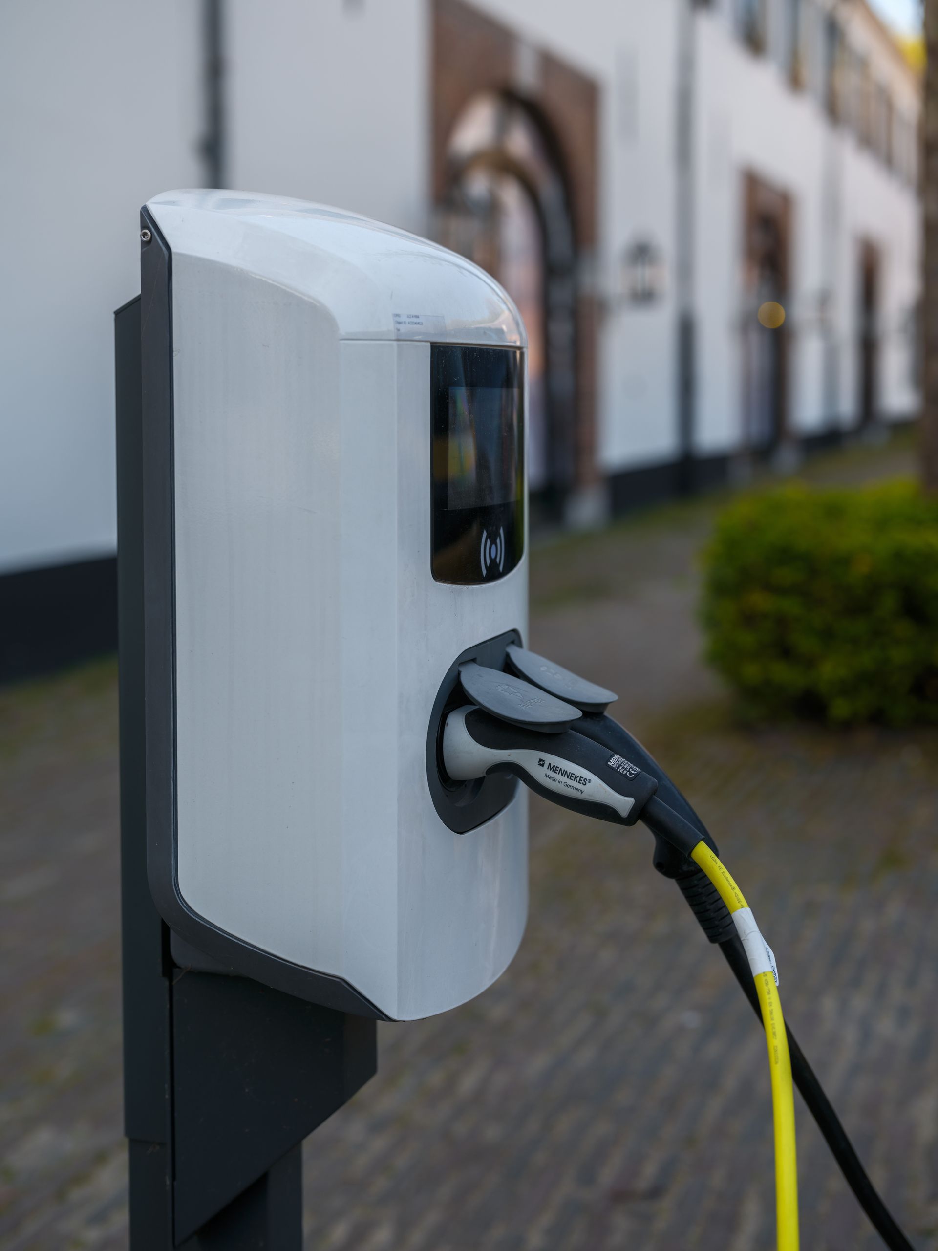 Electric vehicle charging station with plugged-in cable outdoors near a building.