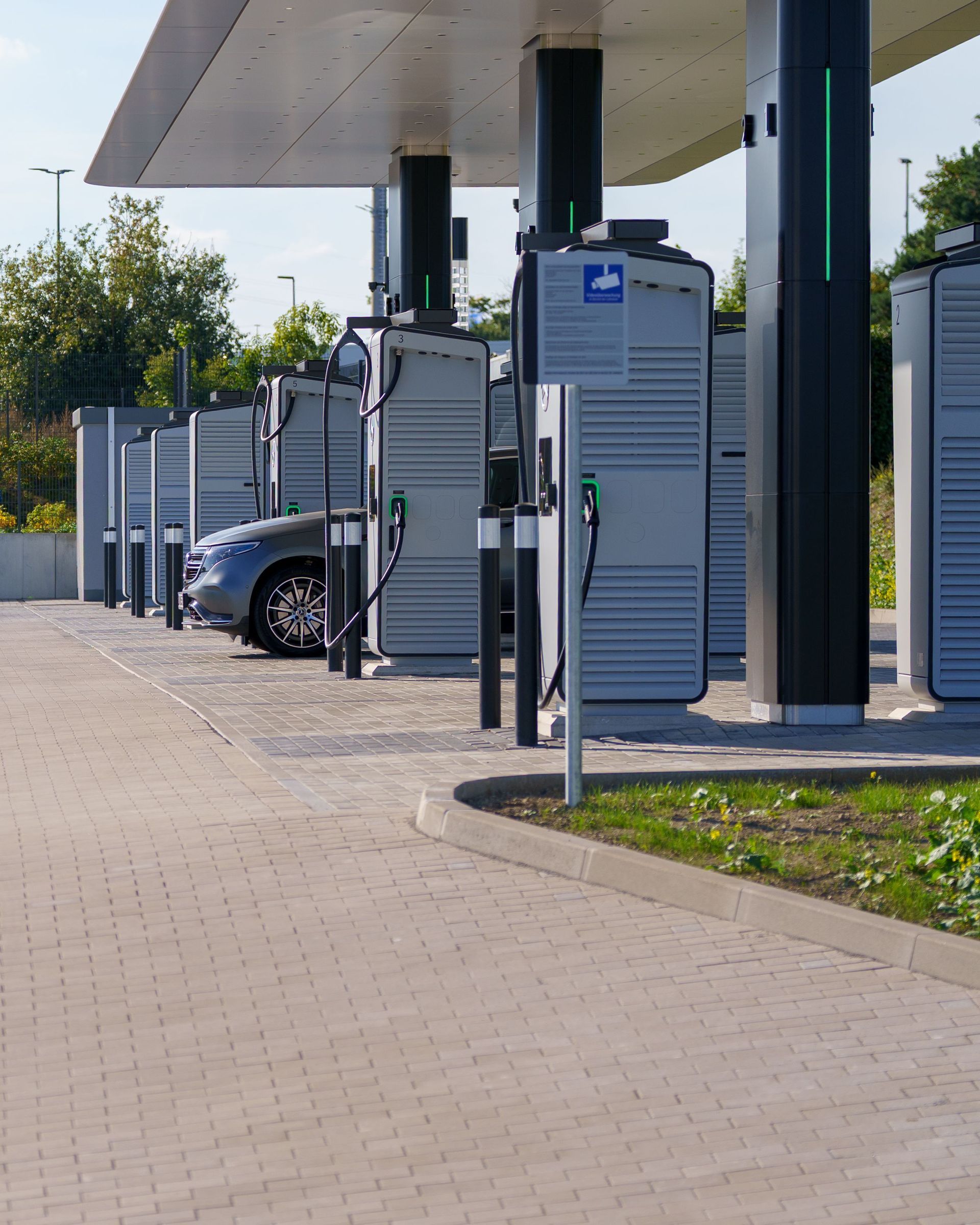 Electric vehicle charging stations under a canopy beside a parked car on a paved lot