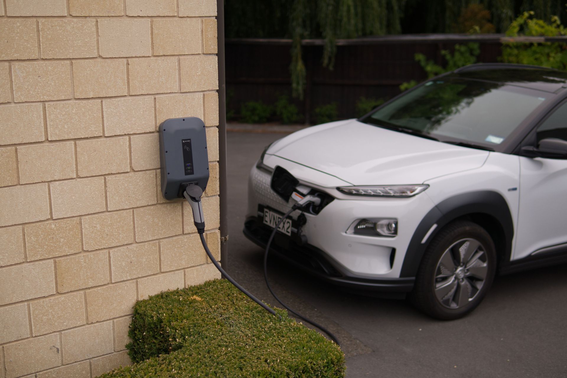 Silver SUV with damaged front bumper parked beside a stone wall and charging station.