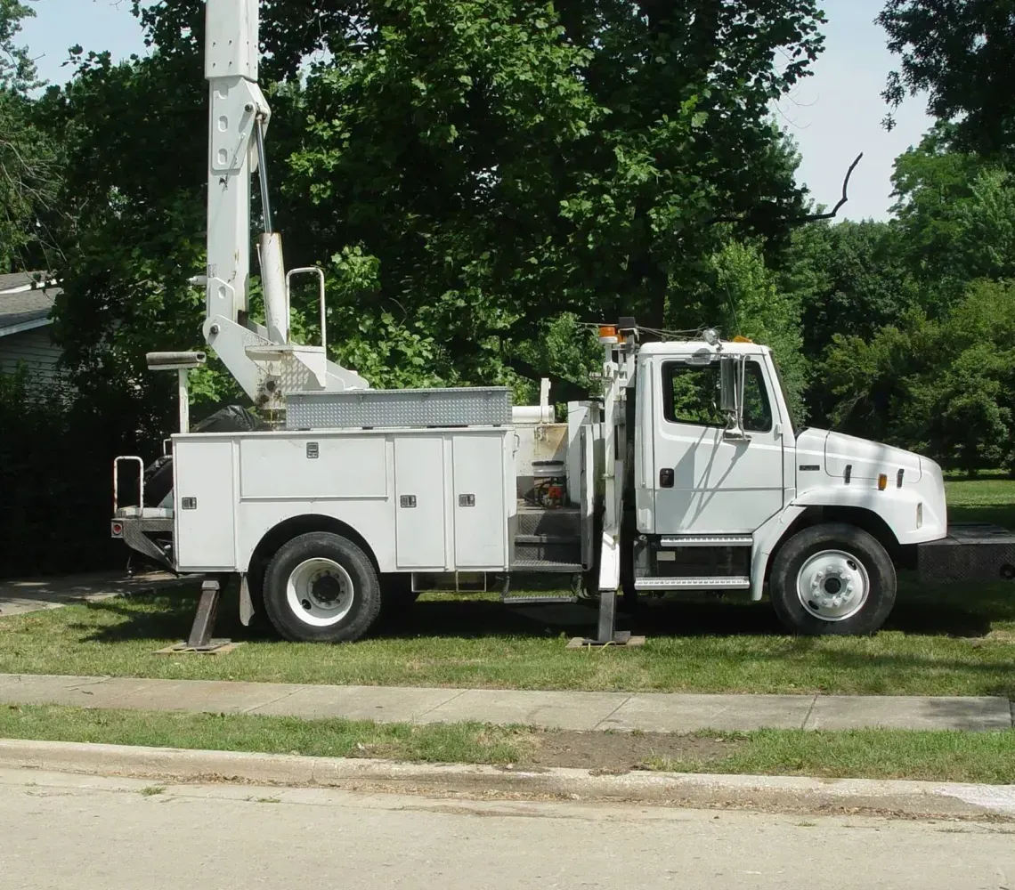 Green utility truck lifting a potted plant with an extended boom arm