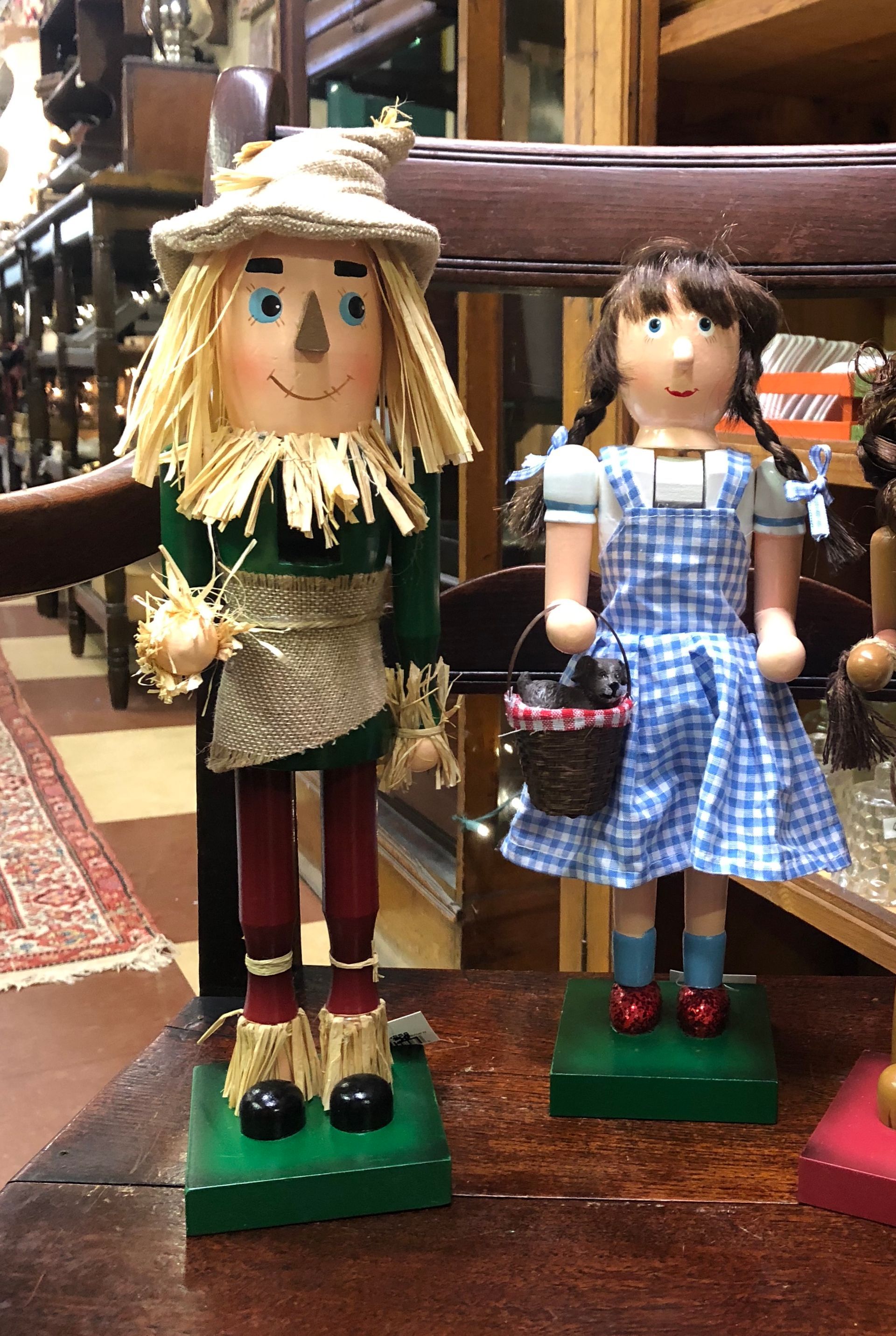 Two handcrafted dolls standing on a table, one in a straw hat and green outfit, one in a blue gingham dress.