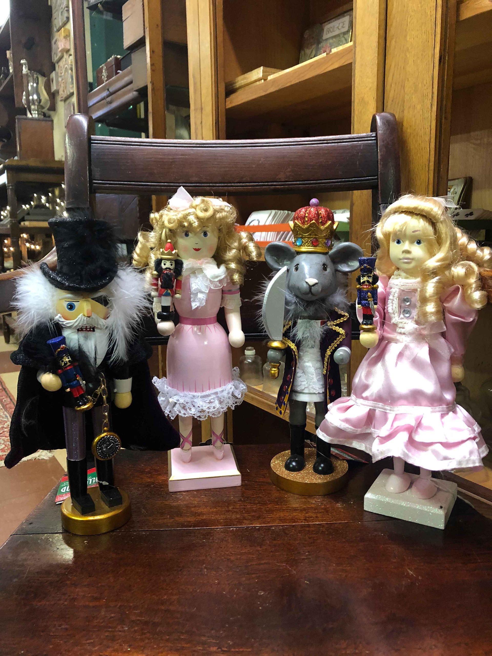 Four small Victorian-style figurines in black, pink, gray, and ruffled pink dresses on a wooden table