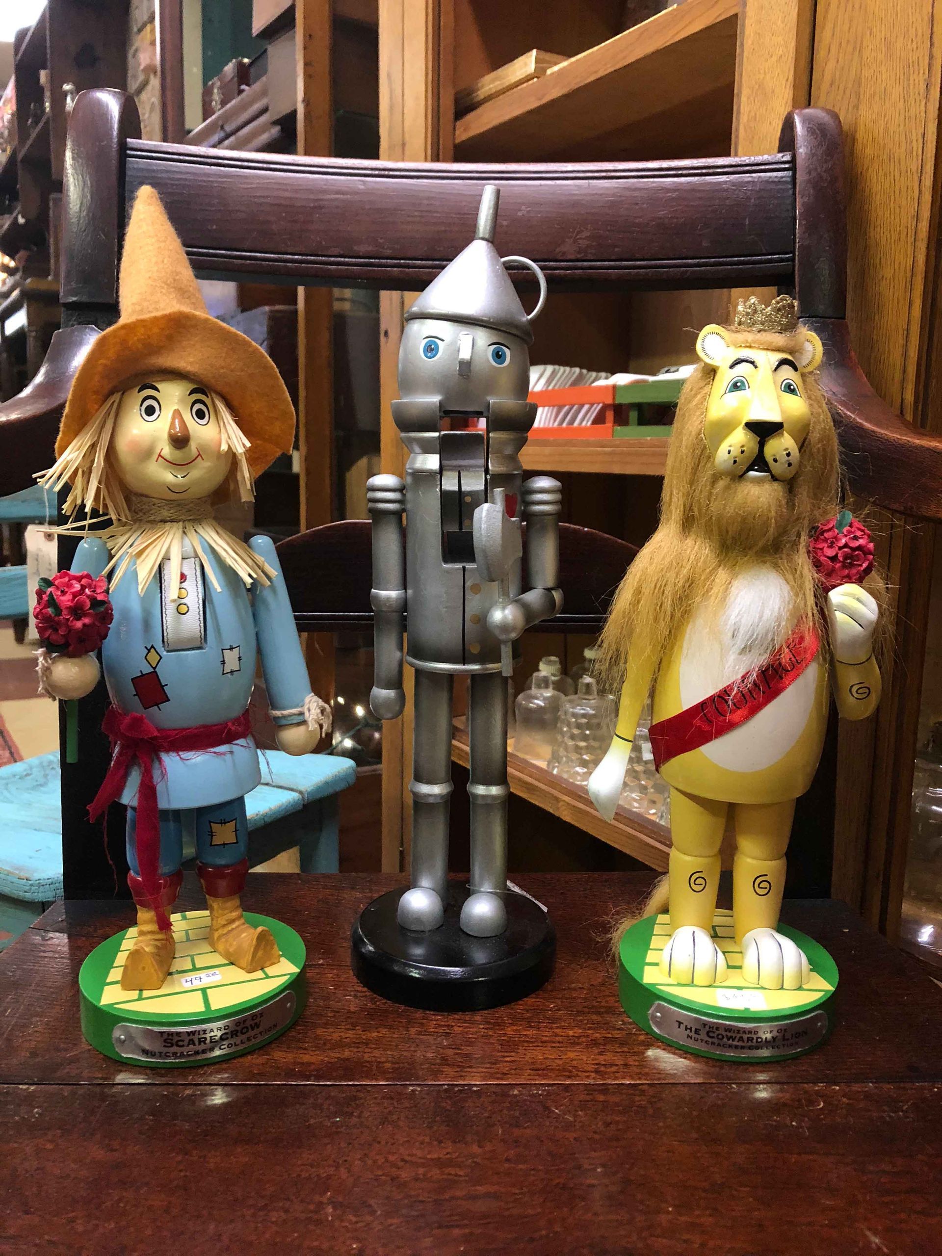 Three Wizard of Oz figurines: scarecrow, tin man, and cowardly lion on a wooden table.