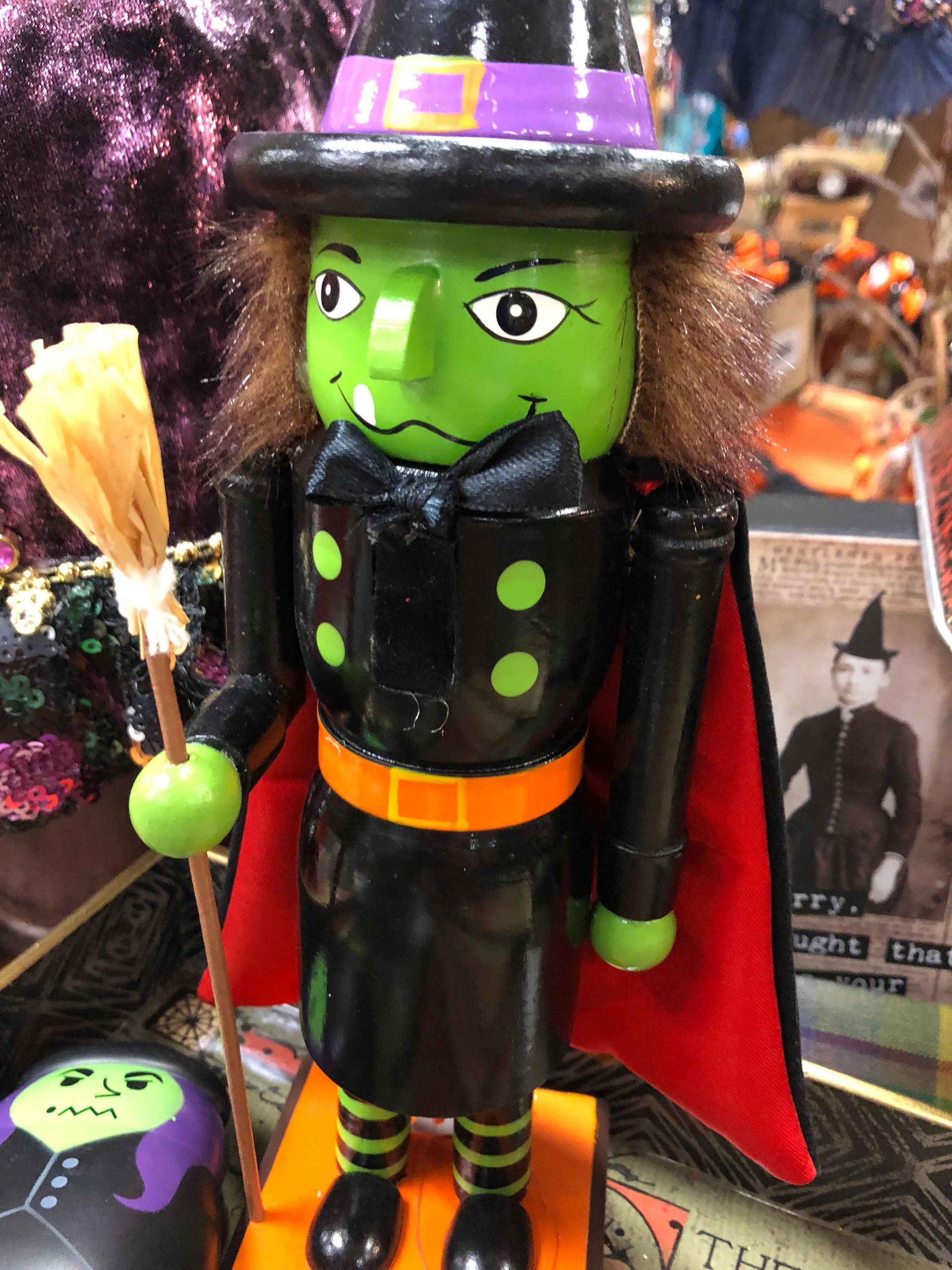 Green witch figurine in black outfit, purple hat, and red cape holding a broomstick for Halloween display