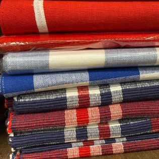 Stacked folded woven blankets in red, blue, gray, and multicolor stripes