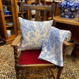 Blue floral cushions on a small wooden armchair in an antique shop.