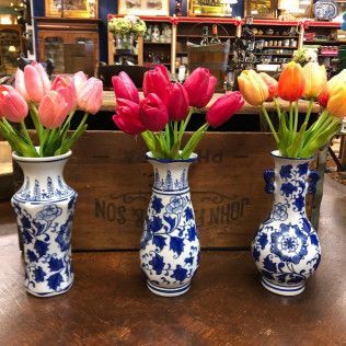 Three blue-and-white vases of colorful tulips on a wooden counter in a shop