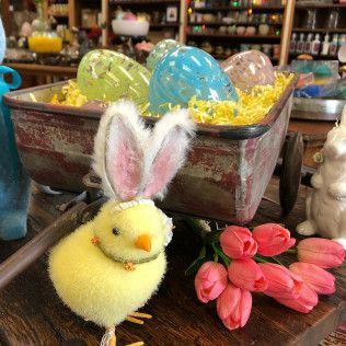 Yellow chick and pink bunny craft figures beside a rustic tray filled with colorful decorated eggs