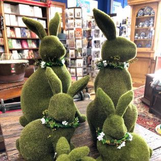 Topiary rabbits in a shop, green moss-like sculptures decorated with small white flowers.