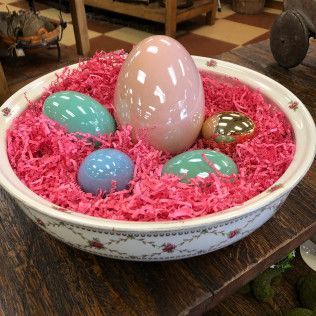Decorative bowl with pastel Easter eggs in pink shredded filler on a wooden table