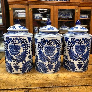 Three blue-and-white porcelain jars with lids on a wooden table in front of a cabinet