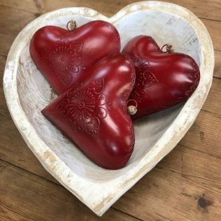 Three red heart-shaped ornaments in a white heart-shaped bowl on a wooden surface