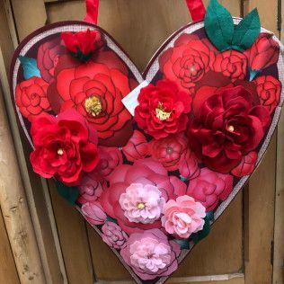 Heart-shaped floral arrangement with red, pink, and white paper flowers against a wooden fence