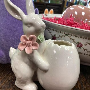 White ceramic bunny planter with pink flower on a wooden table, next to a decorated bowl and purple bunny decoration