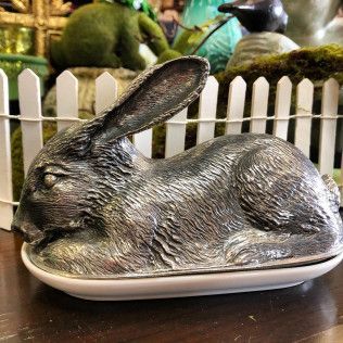 Metal rabbit-shaped dish on a table, with a white picket fence and garden decor behind it.