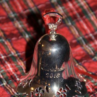 Silver bell ornament with a red handle and engraved “2018” on a red plaid background