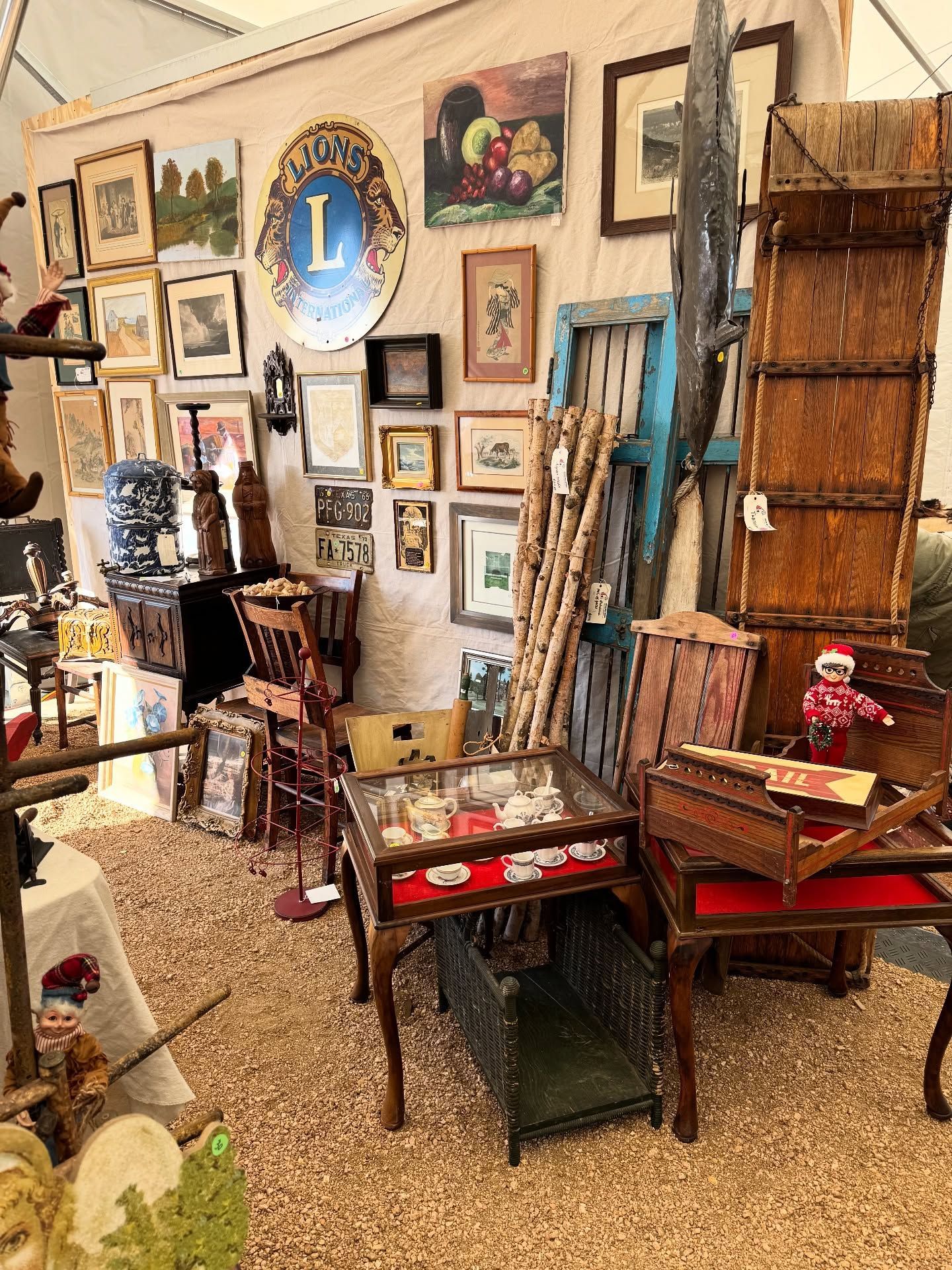 Rustic indoor shop display with framed art, ladders, baskets, and vintage decor on gravel flooring