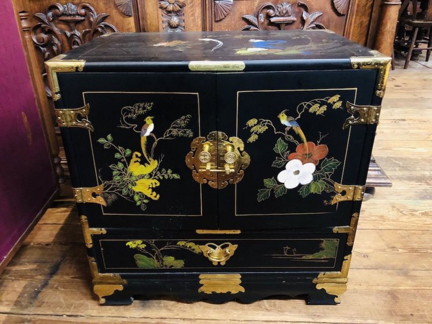 Black lacquered chest with floral inlay and gold hardware on a wooden surface