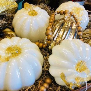 White decorative pumpkins with a gold beaded ornament on straw.