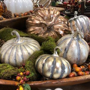 Decorative metallic pumpkins in silver and copper arranged on a rustic display with moss and small gourds
