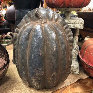 Dark ribbed metal pumpkin-shaped decoration on a shelf with other harvest ornaments