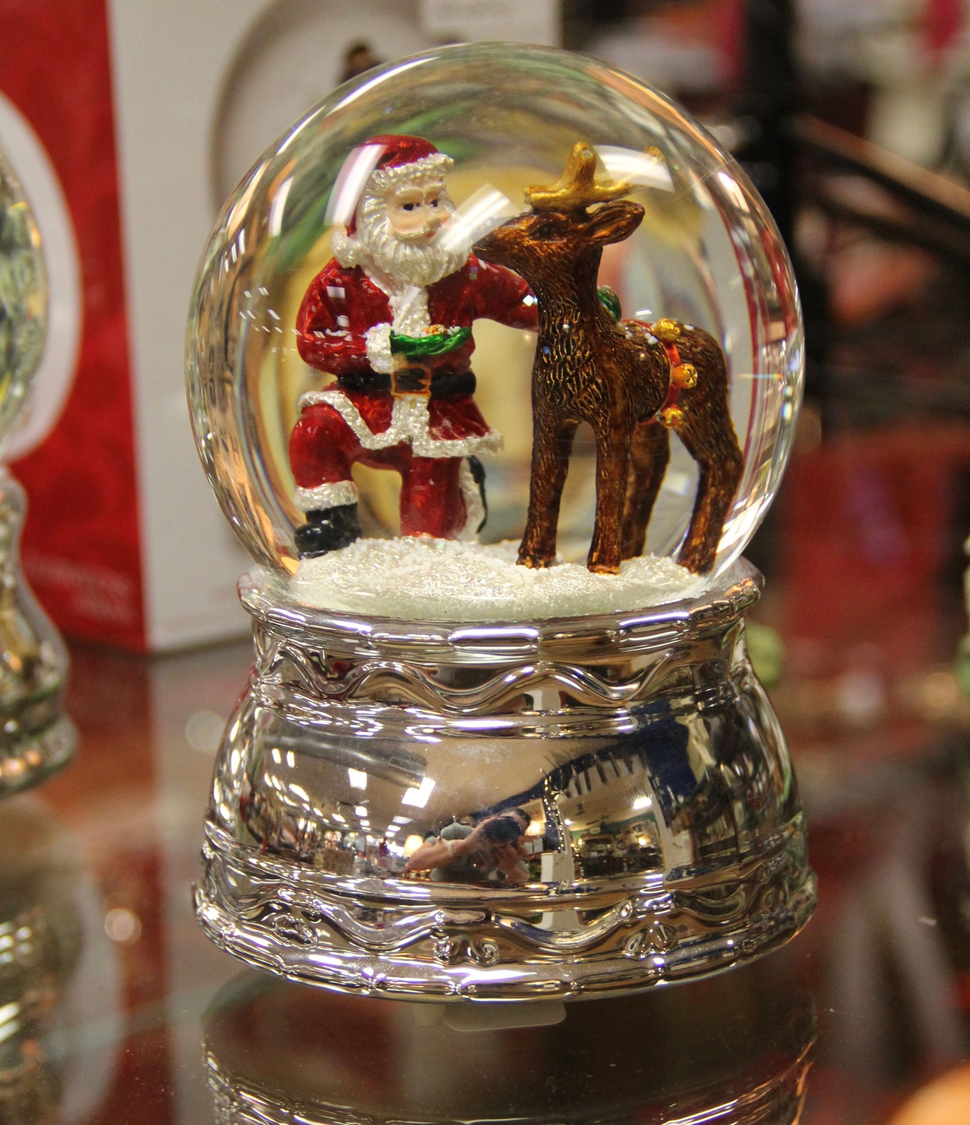 Santa and a reindeer inside a glass snow globe on a reflective base