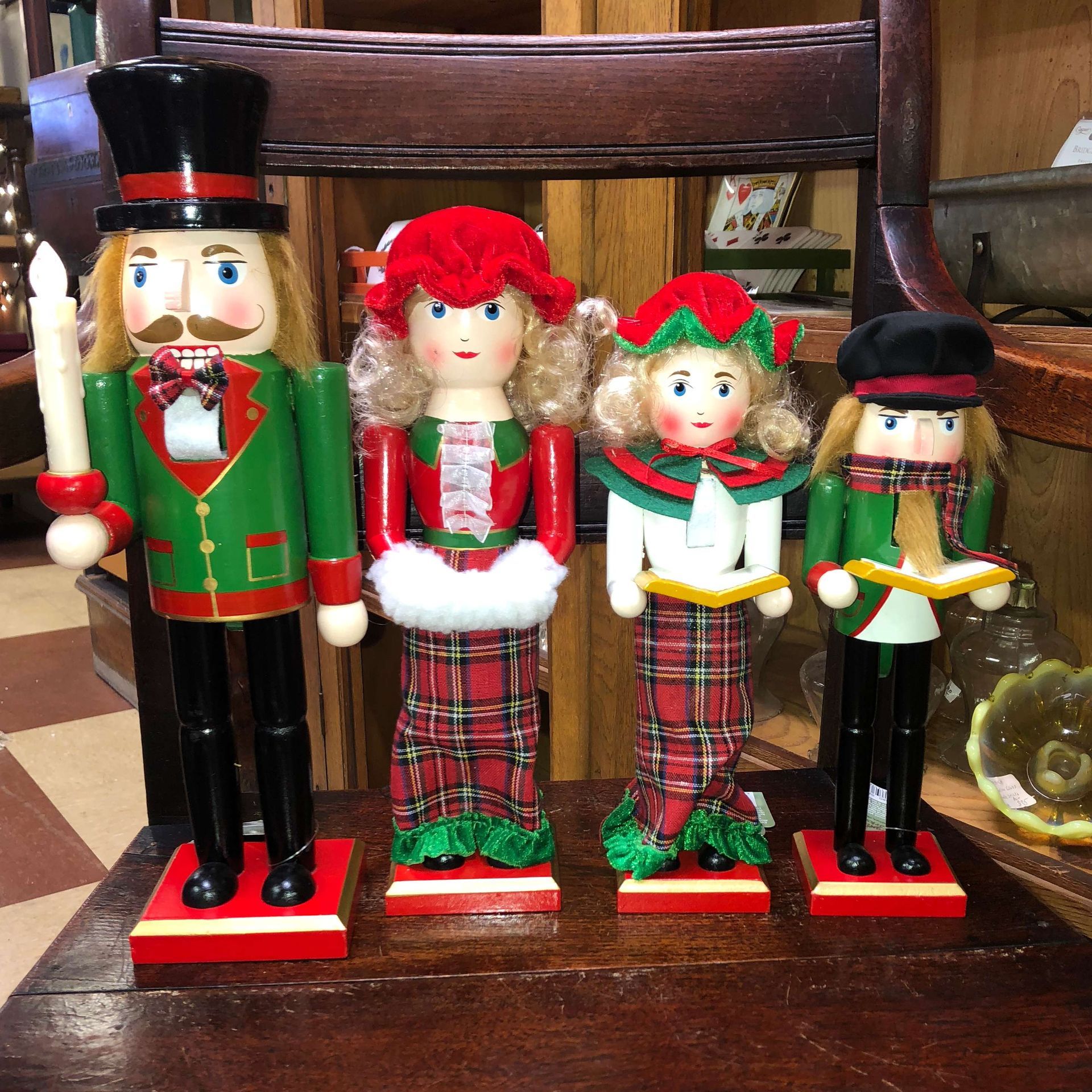 Four Christmas nutcracker dolls on a wooden chair, in red, green, and black holiday outfits.