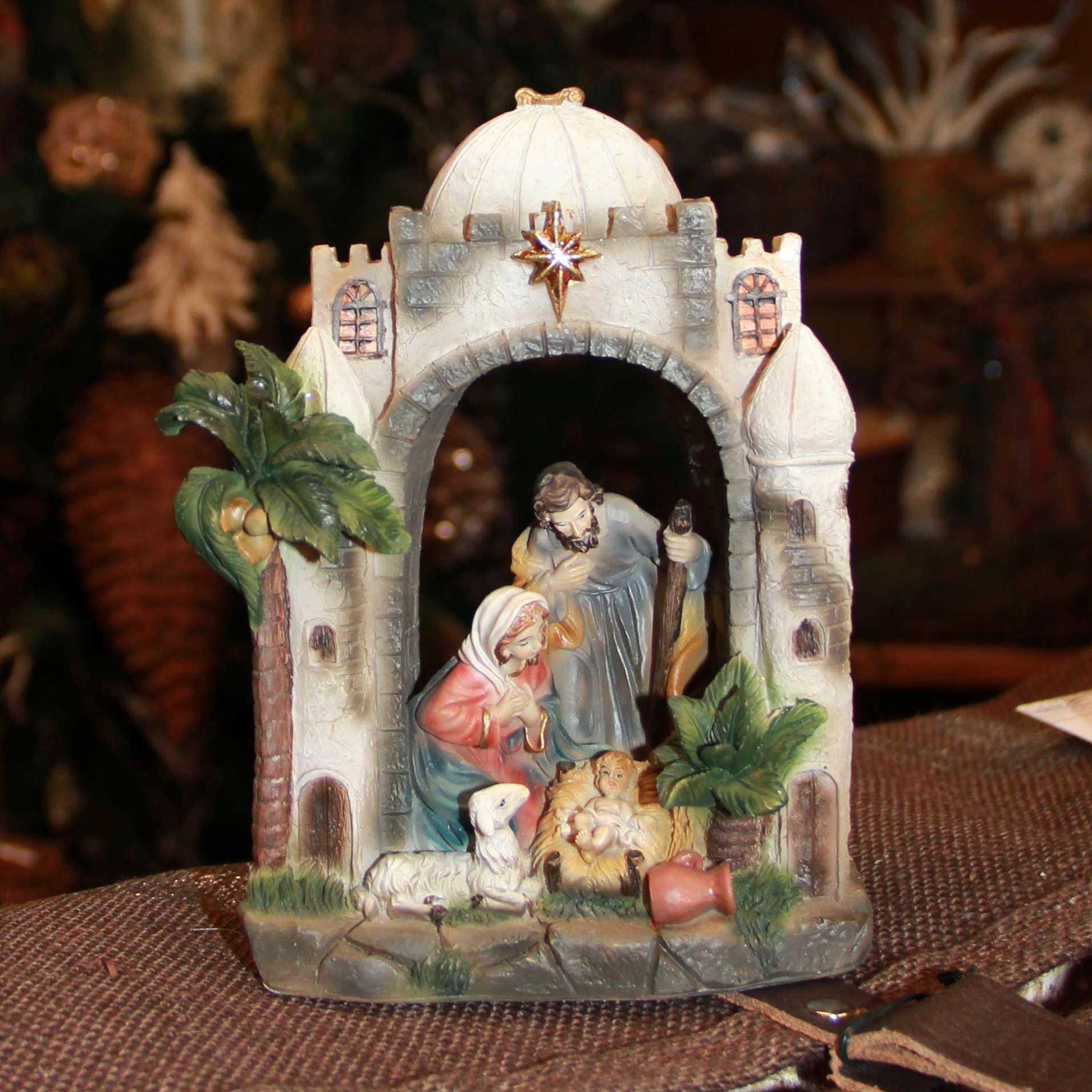 Miniature nativity scene in a white arched stable with figures and palm trees on a table