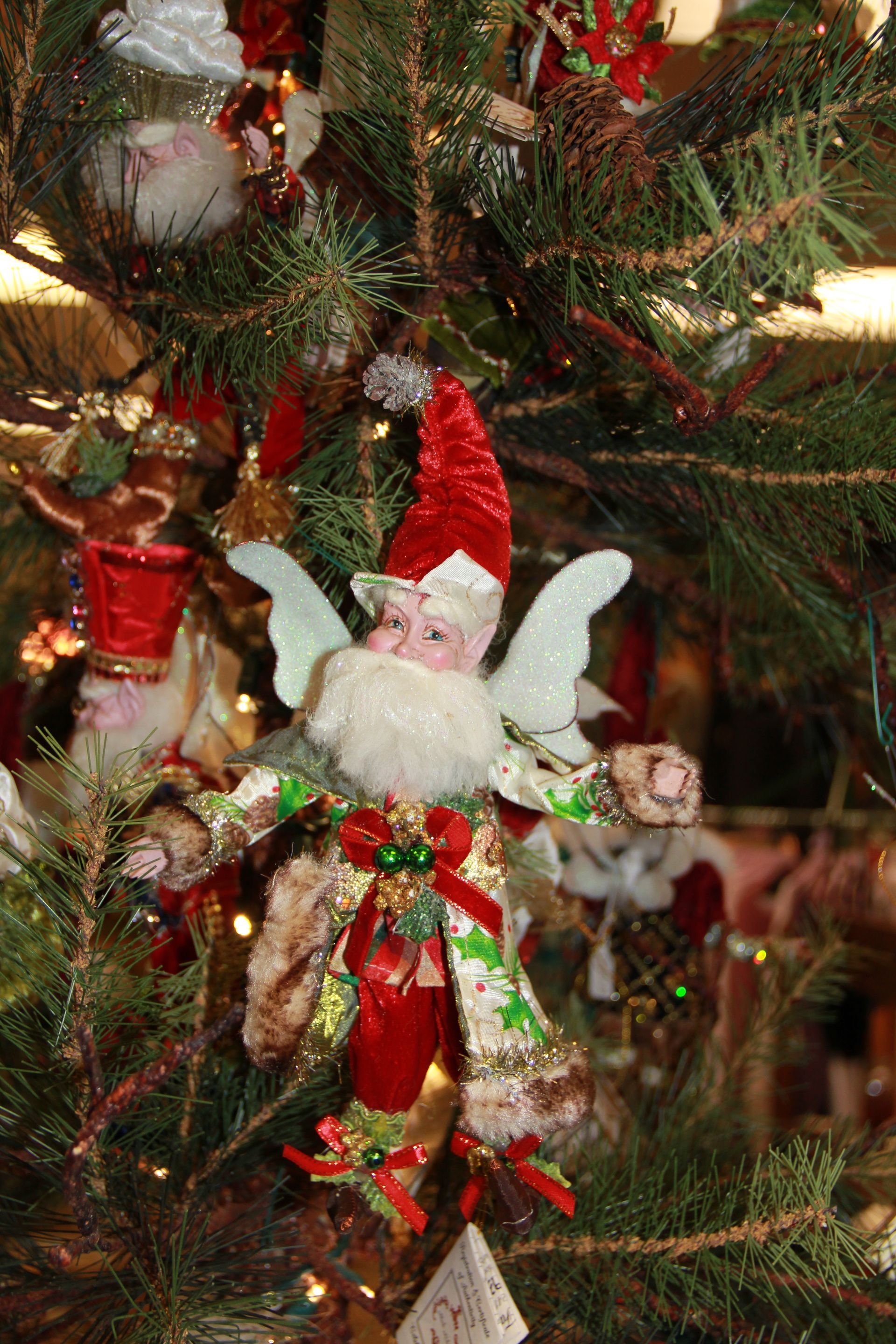 Christmas tree ornament of a red-and-white fairy with wings and a green dress hanging among branches
