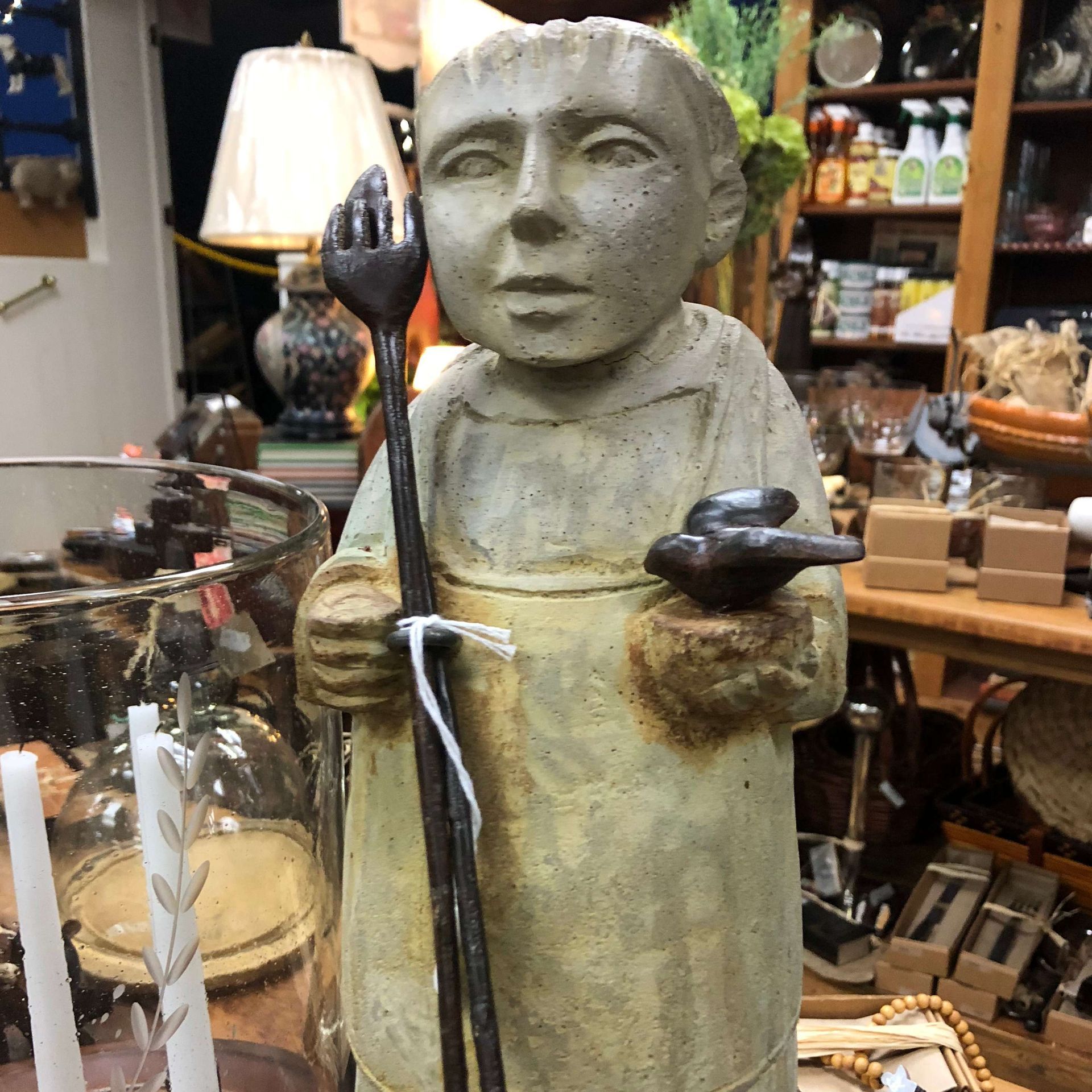Weathered stone statue of a robed figure holding a staff and bowl in a shop display