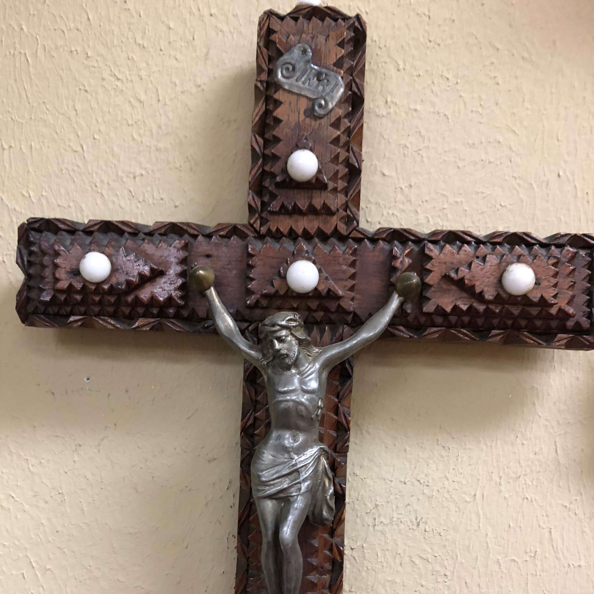 Decorative wooden wall cross with silver crucifix and white bead accents on a beige wall