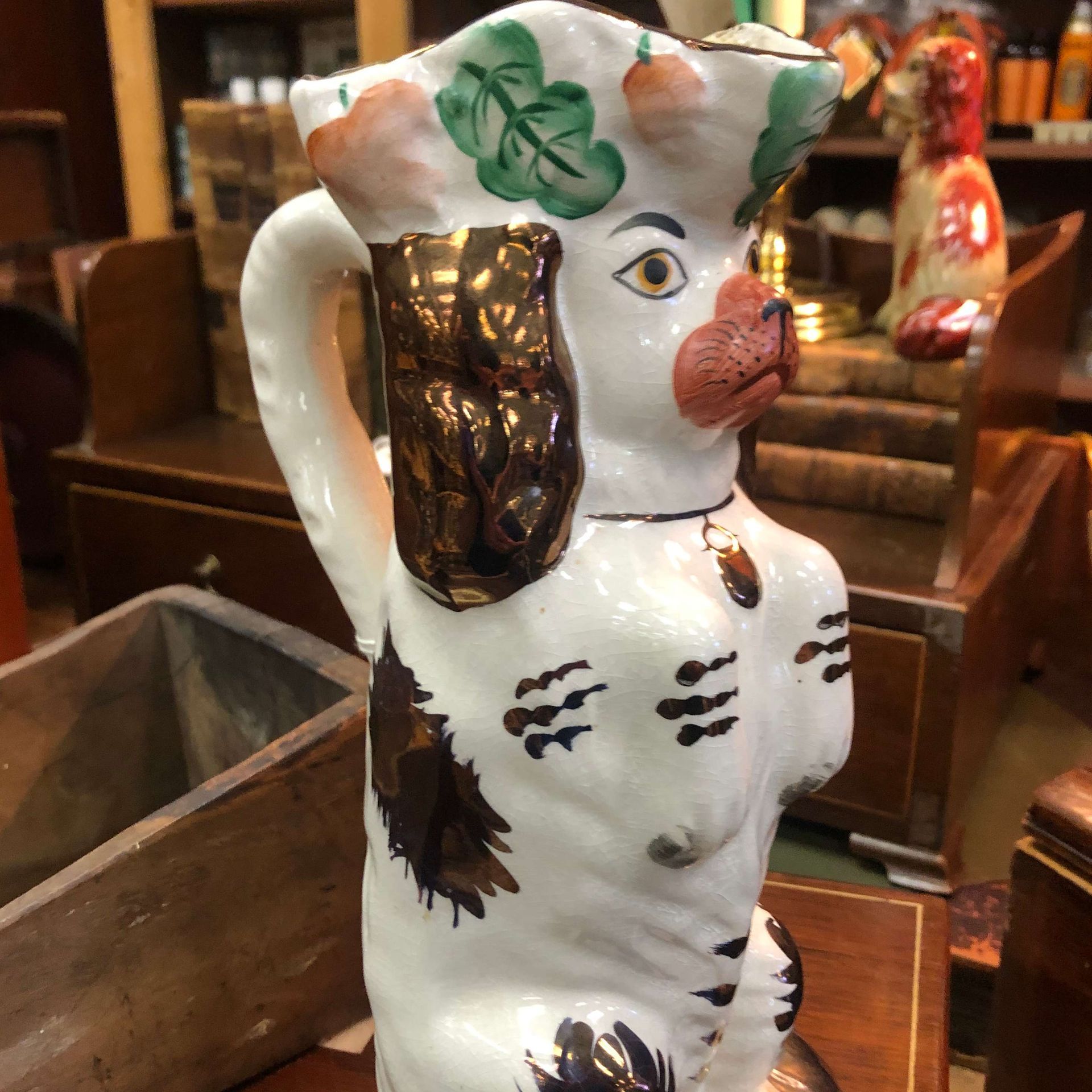 Ceramic dog-shaped pitcher with white glaze and brown accents on a wooden shelf