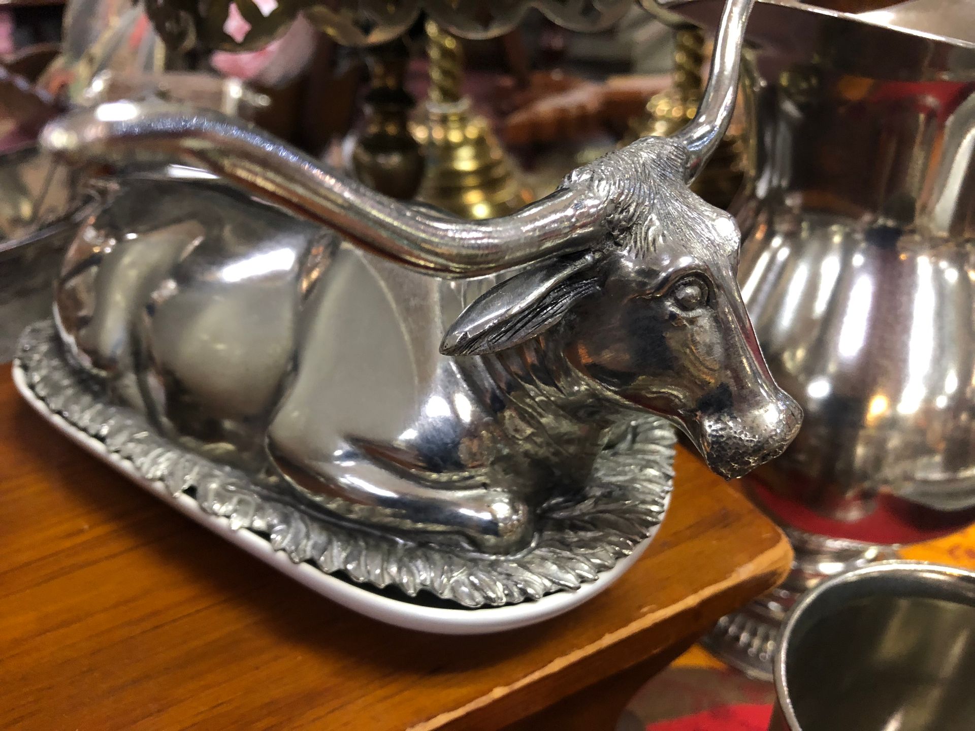 Silver bull-shaped dish or napkin holder on a wooden table, with reflective metal pitchers in the background
