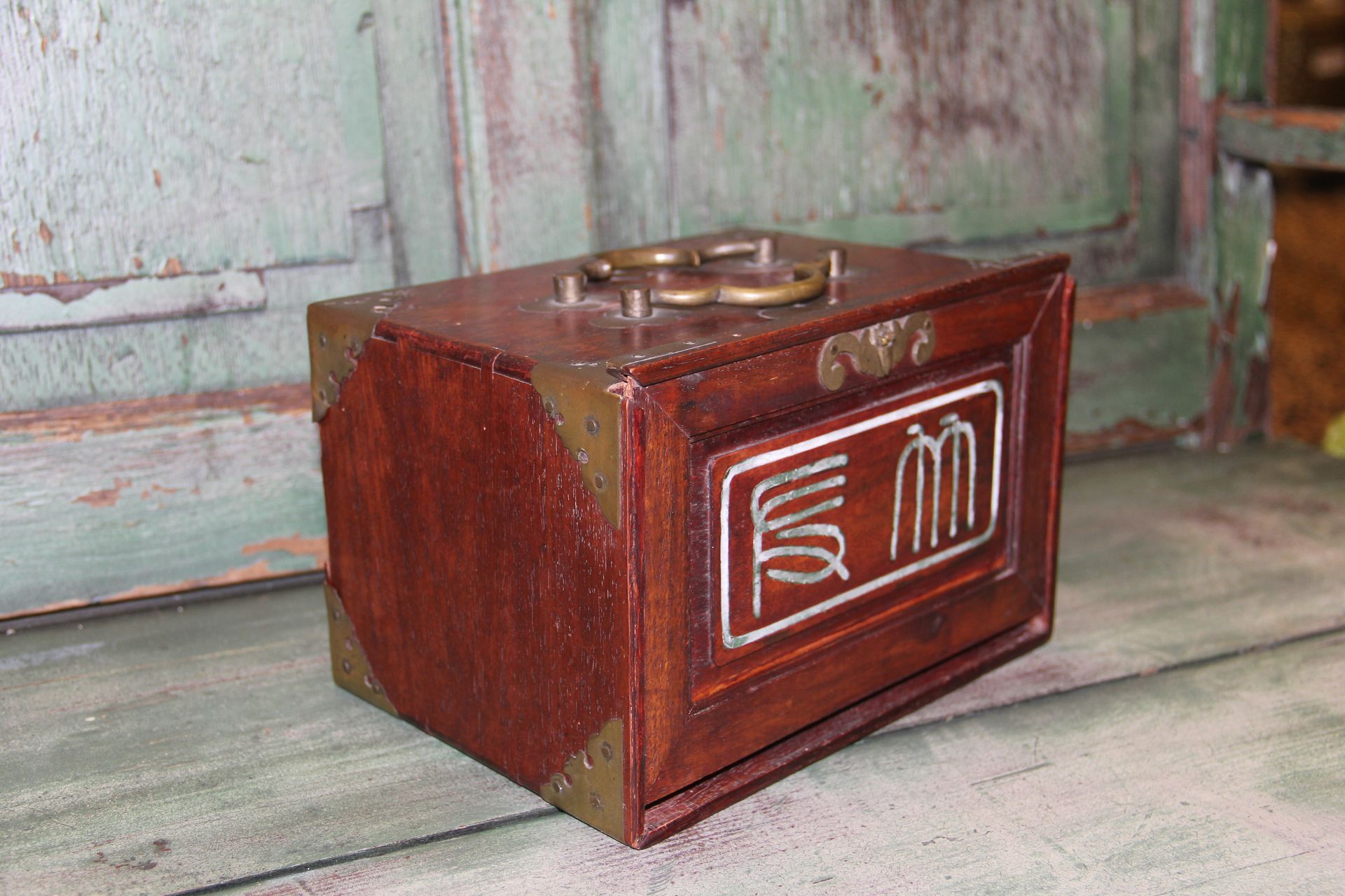 Small brown wooden box with a carved decorative front panel, sitting on a weathered floor.