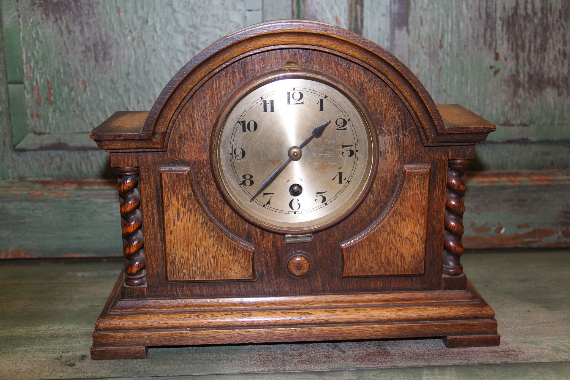 Antique wooden mantel clock with a round white face on a rustic surface.