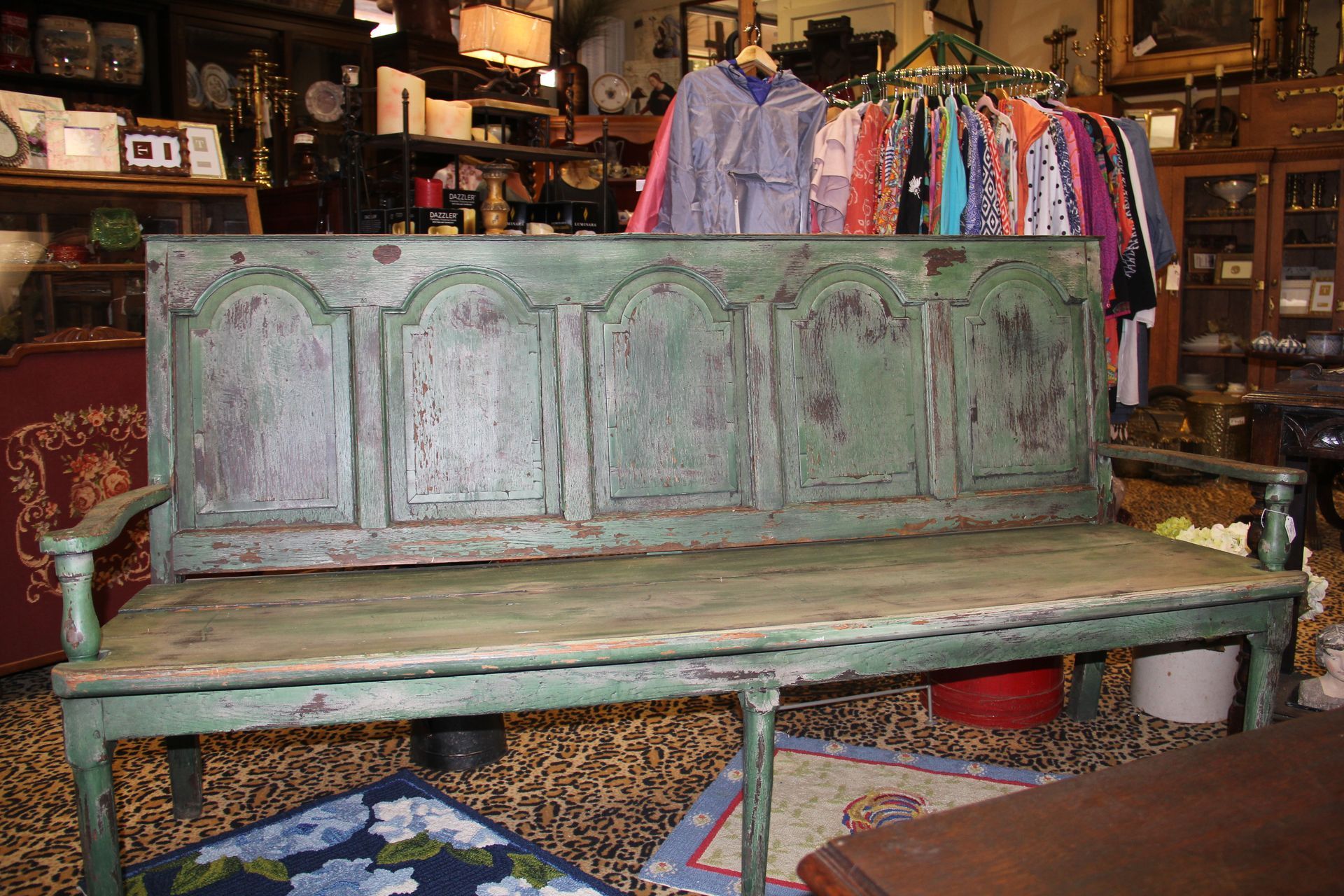 Distressed green wooden bench with ornate backrest in a cluttered antique shop