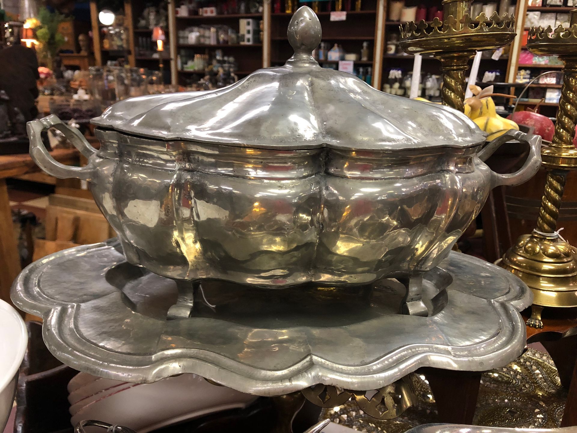 Shiny silver lidded serving bowl on a decorative stand in a shop display