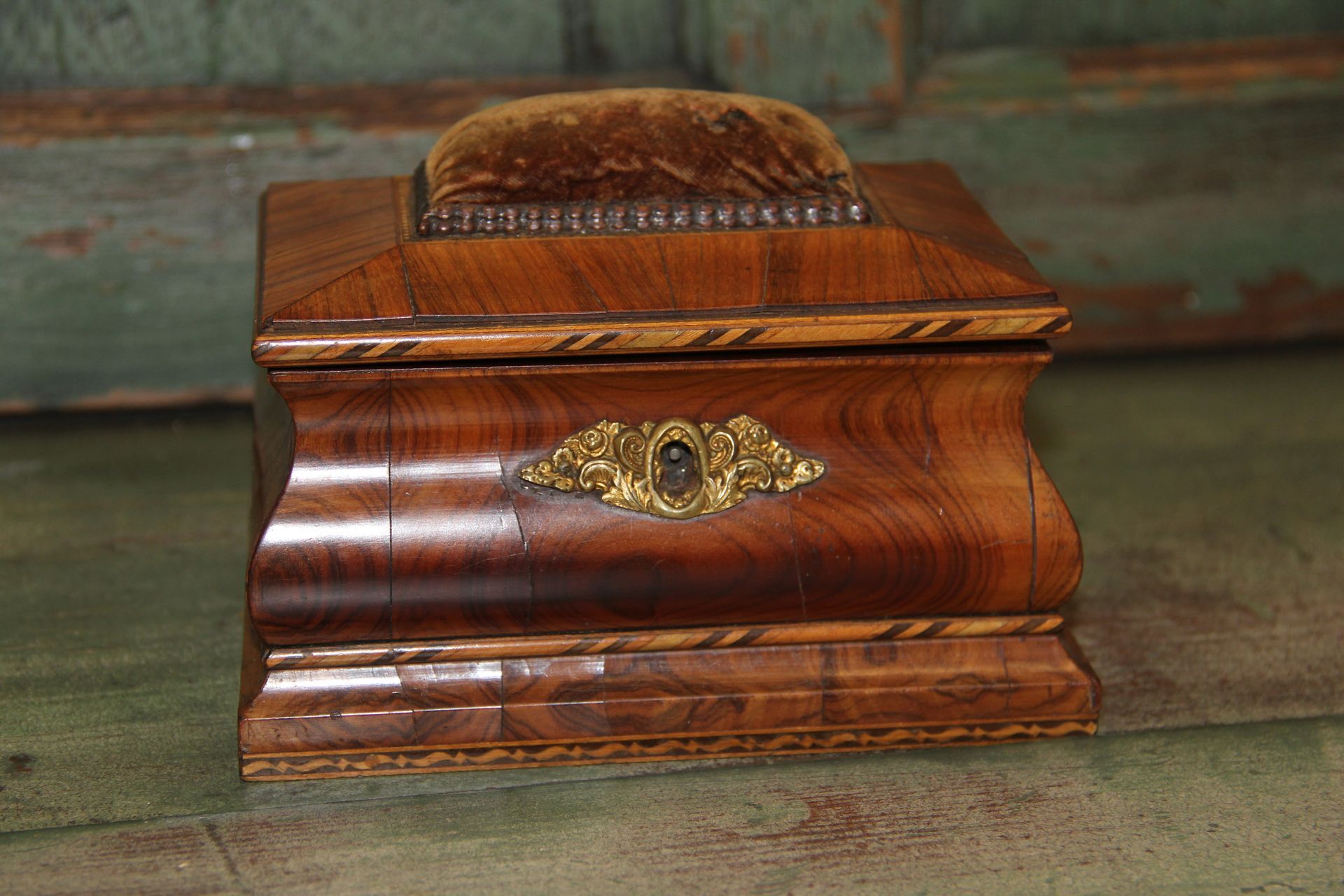 Small polished wooden box with a brass ornament on a worn green surface.
