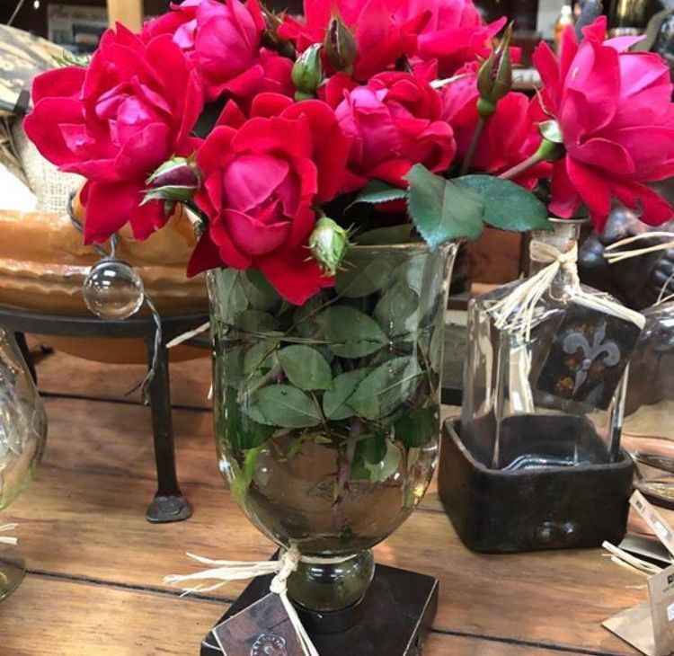 Red roses arranged in a glass vase on a wooden table with other decorative items nearby