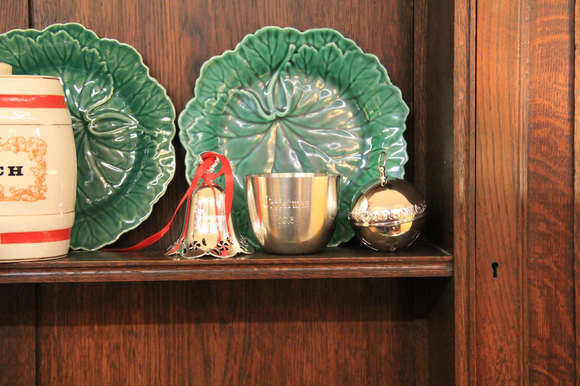Green decorative plates, small cups, and a bell arranged on a wooden shelf.