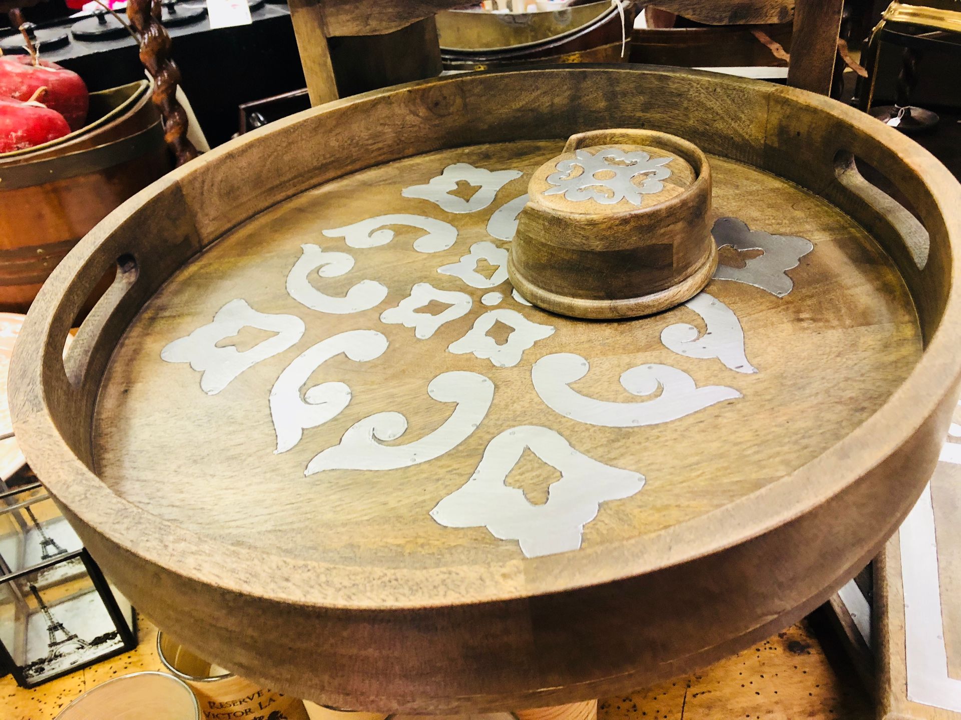 Round wooden tray with white floral designs and a small cup in the center, displayed on a table.